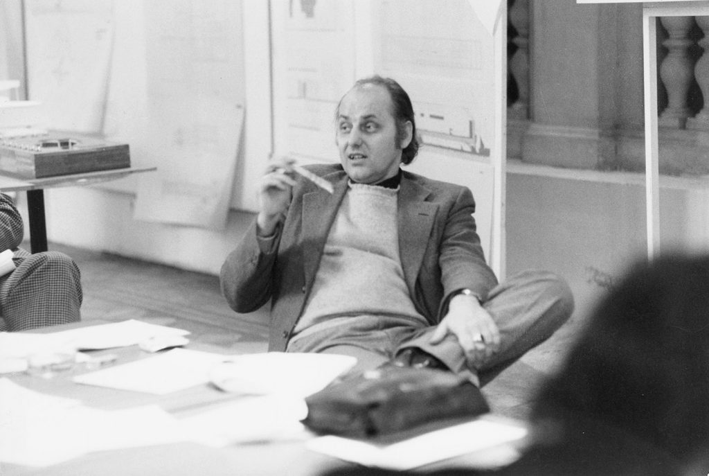 black and white photo with man holding something in his hand and sitting in front of a table with many pieces of paper