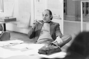 black and white photo with man holding something in his hand and sitting in front of a table with many pieces of paper