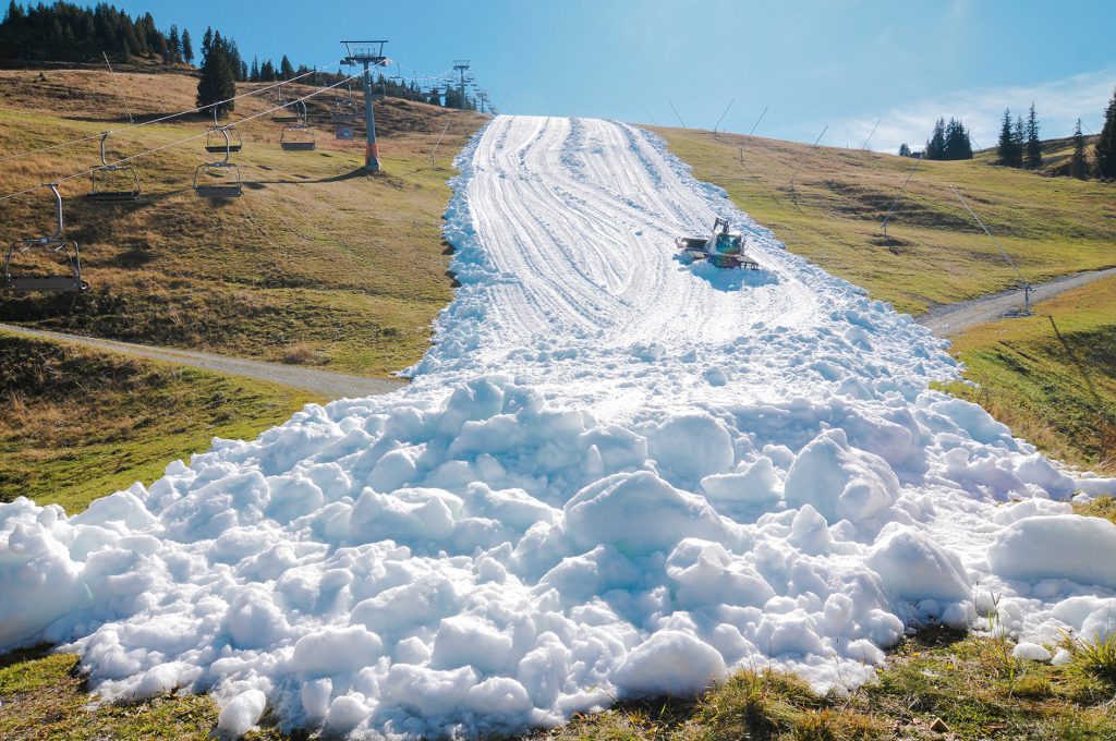 Schnee auf einer grünen Almwiese, daneben ein Seesellift