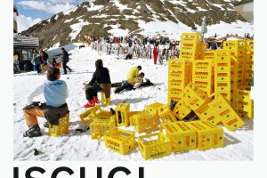 viele gelbe Kisten liegen auf einer schneebedecketen Wiese und dahinter viele Menschen mit Skiern