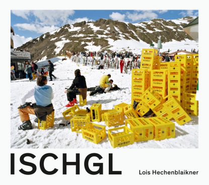 viele gelbe Kisten liegen auf einer schneebedecketen Wiese und dahinter viele Menschen mit Skiern