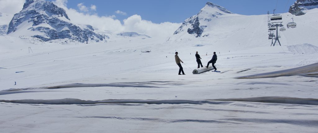 3 Personen auf einer schneebedeckten hochalpinen Landschaft, die eine Rolle gemeinsam ziehen