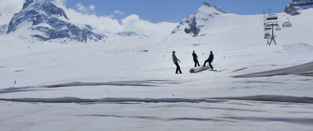 3 people on a snow-covered high alpine landscape pulling a roller together