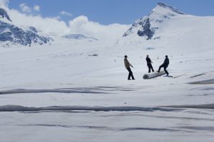 3 people on a snow-covered high alpine landscape pulling a roller together