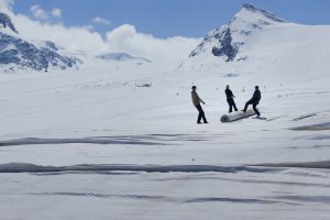 3 Personen auf einer schneebedeckten hochalpinen Landschaft, die eine Rolle gemeinsam ziehen