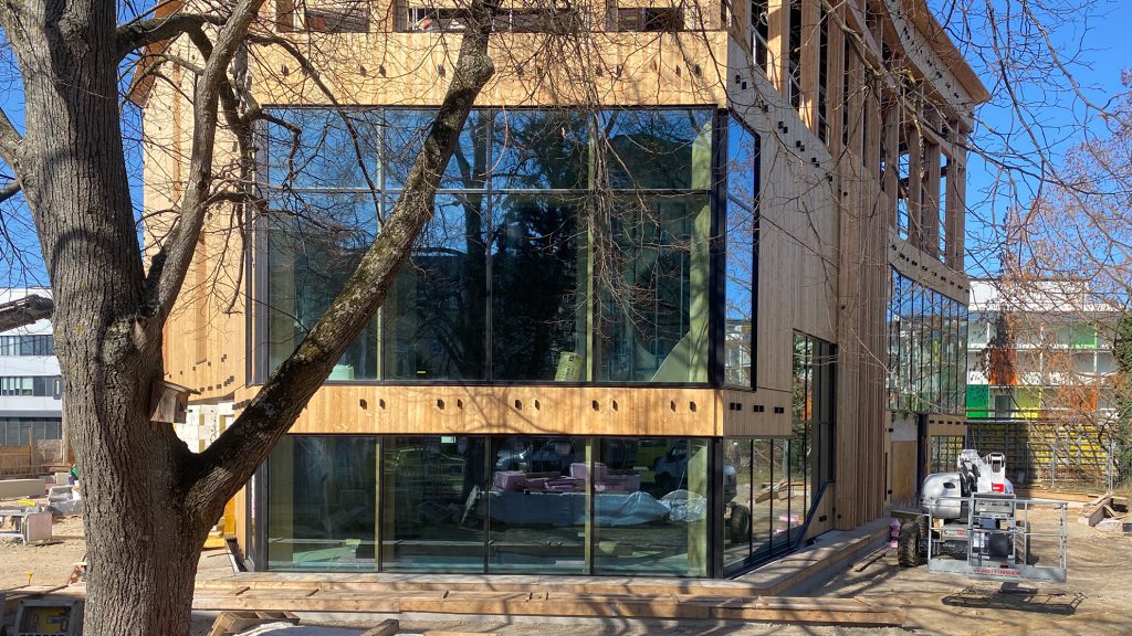 Building with large glass windows and wooden façade, with a tree in front of it