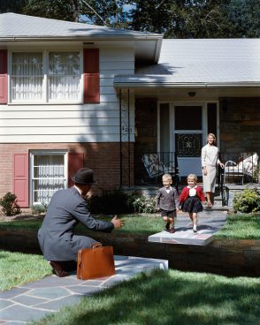 Woman standing in the background, in front of her two small children running towards a man