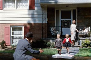 Woman standing in the background, in front of her two small children running towards a man