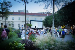 Courtyard with plants in the foreground, people looking at a screen behind them