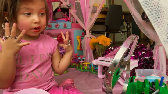 kleines Mädchen in rosa gekleidet hält die Hände mit vielen Ringen nach oben 