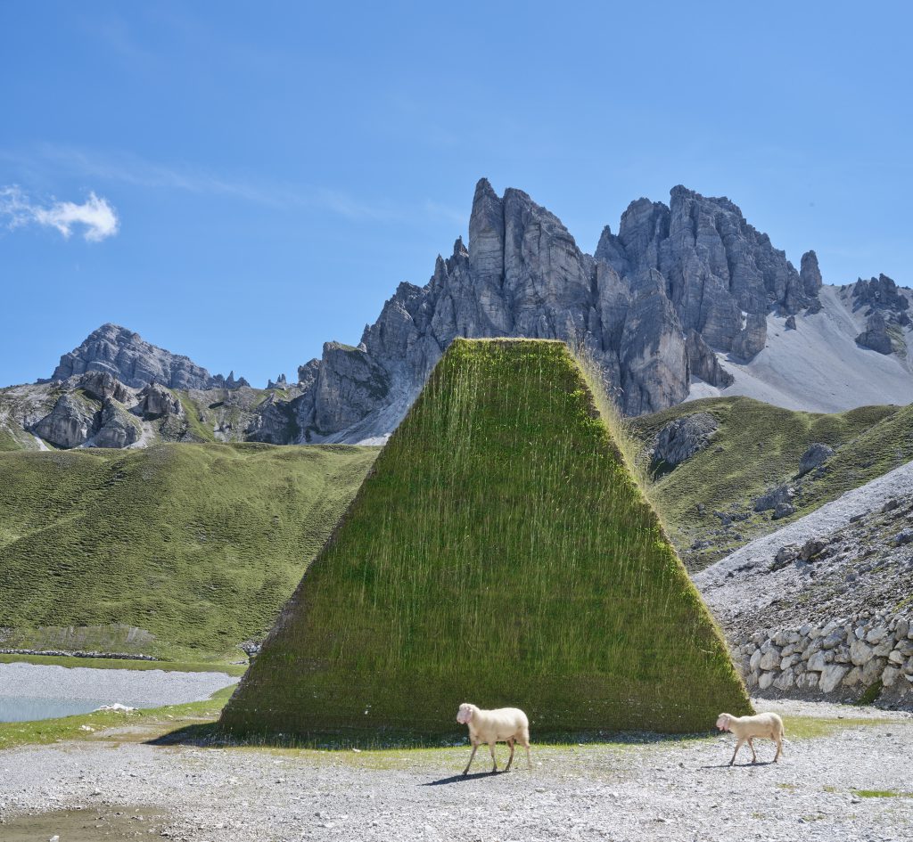 High mountains in the background, sheep in front of a pyramid-like tower of grass