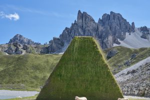 High mountains in the background, sheep in front of a pyramid-like tower of grass