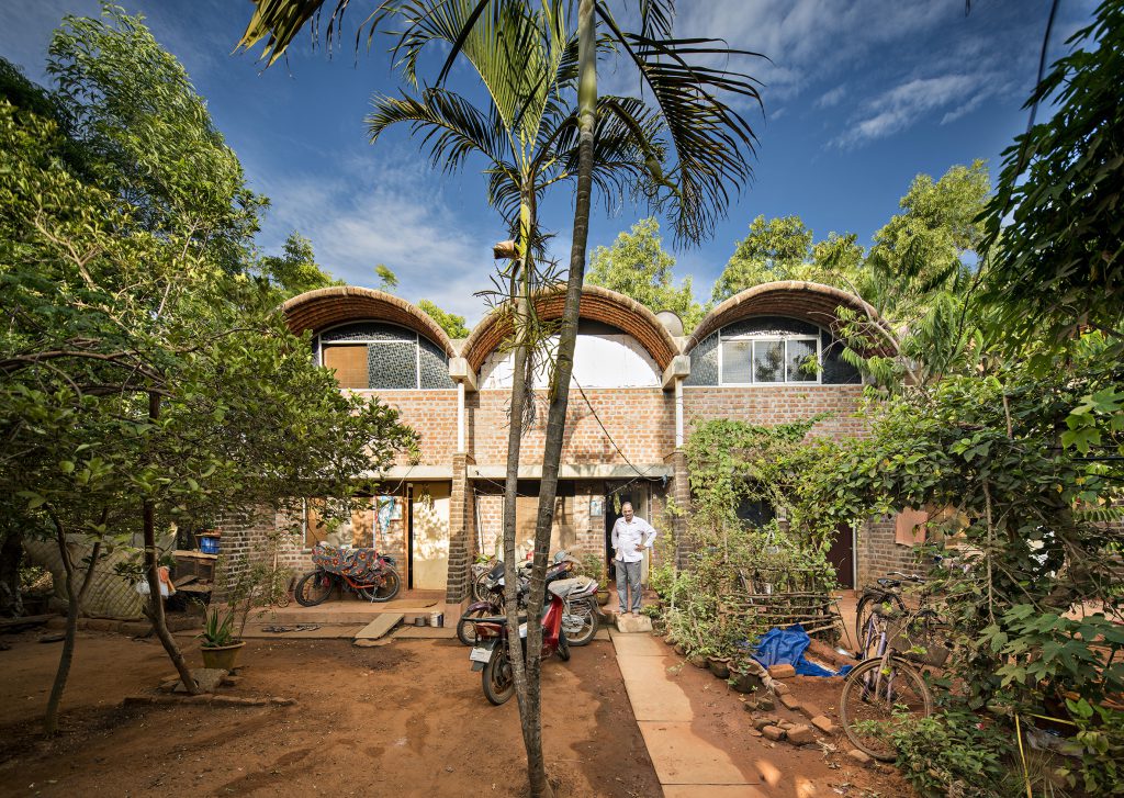Palme, dahinter Gebäude mit gewölbten Dächern, im Vordergrund ein paar Motorräder