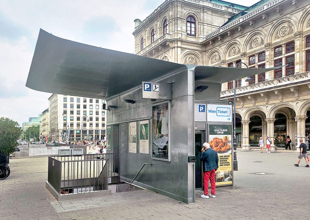 Gebäude mit einem Metall-Flügeldach das vor einem großen alten Gebäude steht