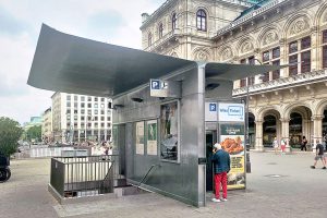 Gebäude mit einem Metall-Flügeldach das vor einem großen alten Gebäude steht