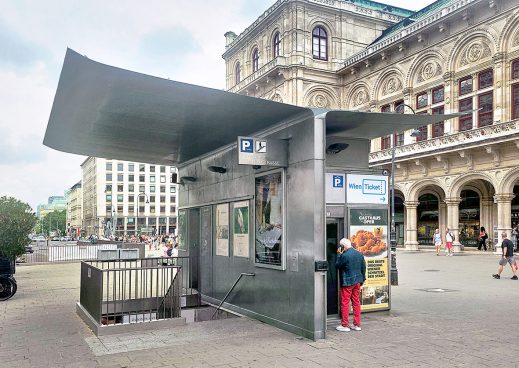 Gebäude mit einem Metall-Flügeldach das vor einem großen alten Gebäude steht