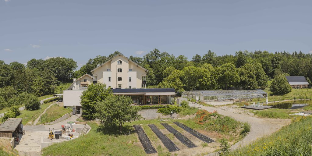 Haus mit große, Garten davor und einigen Glashäusern rechts im Hintergrund