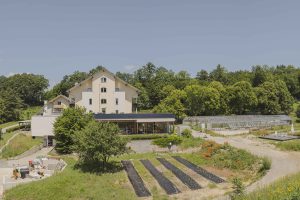 Haus mit große, Garten davor und einigen Glashäusern rechts im Hintergrund