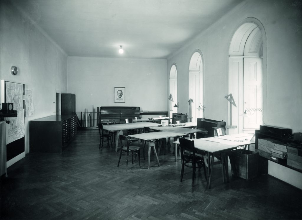 s/w Foto mit Raum mit Tischen, Rundbogenfenstern und einem Foto an der hinteren Wand