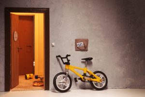 gelbes Kinderfahrrad steht vor einer offen Tür angelehnt an eine Wand