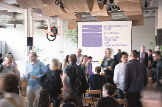 A room filled with people, with a screen mounted in the background displaying the words