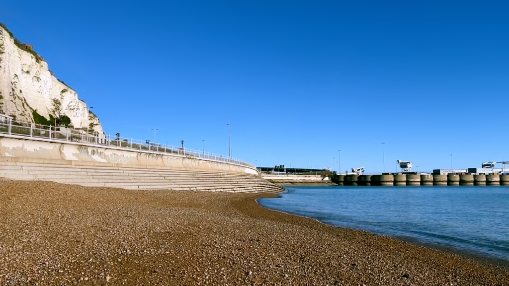 Strand mit Stufen zum Wasser und zum Sand, oberhalb eine Straße und ein heller Felsen