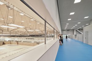 riesige Indoor-Turnhalle mit einem Gang (blauer Boden) und Fensterscheiben wo man hindurchschauen kann