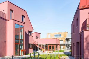mehrere nebeneinanderstehende rosrote Häuser, dazwischen eine Wiese