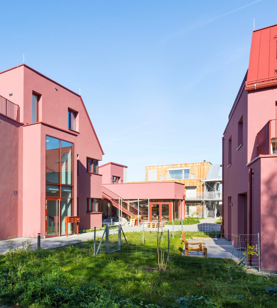 mehrere nebeneinanderstehende rosrote Häuser, dazwischen eine Wiese