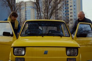 2 people who are getting into or out of a yellow car