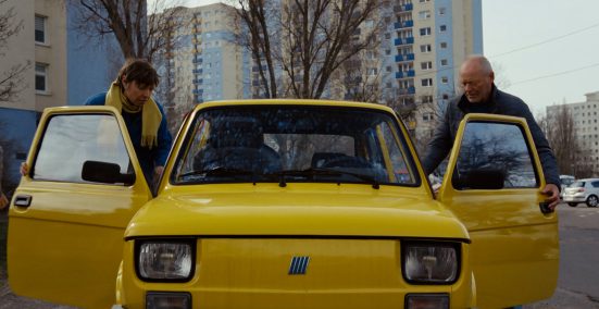 2 people who are getting into or out of a yellow car