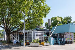 ein Gebäude mit hellblauem Dach und Gitter. Es ist mit einem Bauzaun eingezäunt. Im Hintergrund sieht man das Riesenrad.