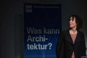 © Foto: eSeL eine Frau mit dunklen gelockten Haaren schaut nach rechts, dahinter ist ein Schriftzug zu sehen