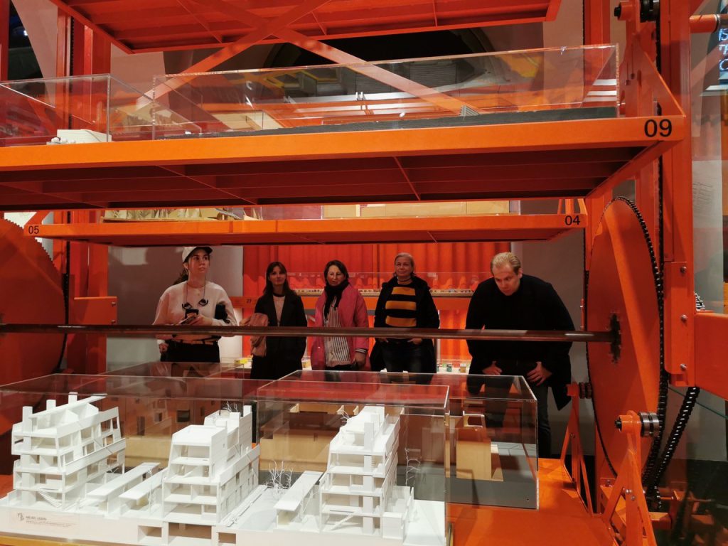 5 Personen stehen vor einem roten Gerüst auf dem sich mehrere Architekturmodelle befinden